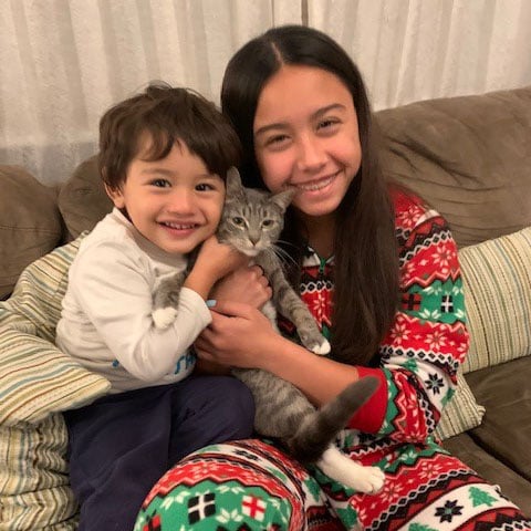 a girl and a boy sitting on a couch holding a cat
