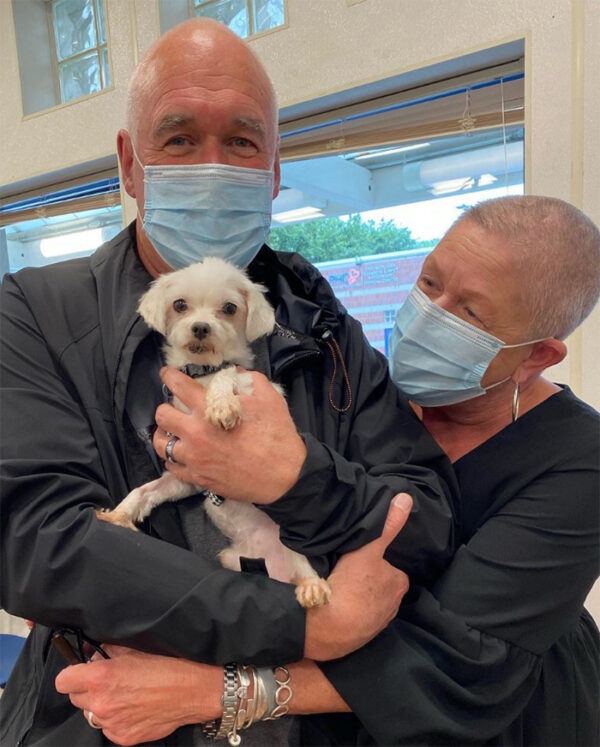 a man and woman wearing face masks holding a dog