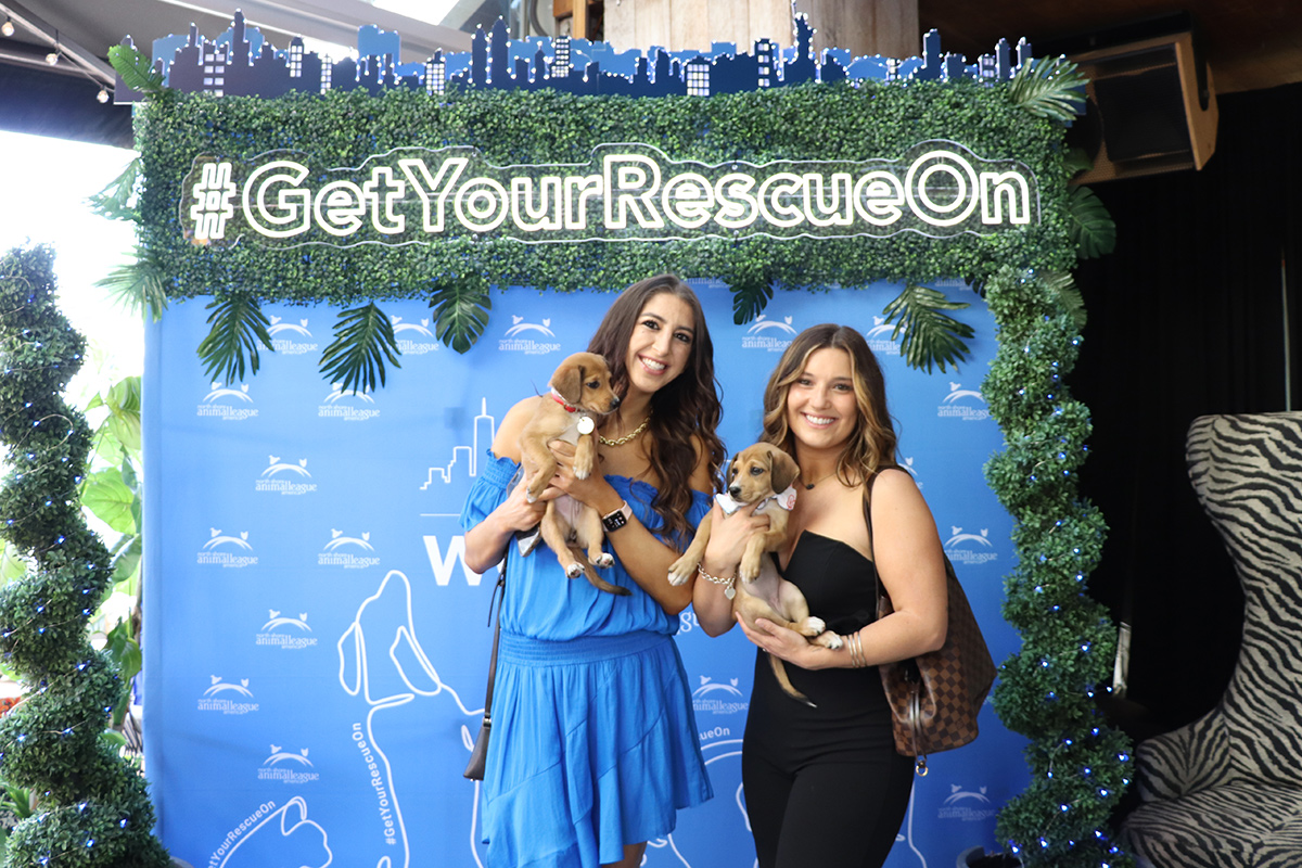 two women holding puppies in front of a sign